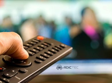 Diferencia entre Android TV y Google TV: ¿Cuál es el adecuado para ti? 5 Mano sujetando un mando a distancia con una televisión desenfocada de fondo.