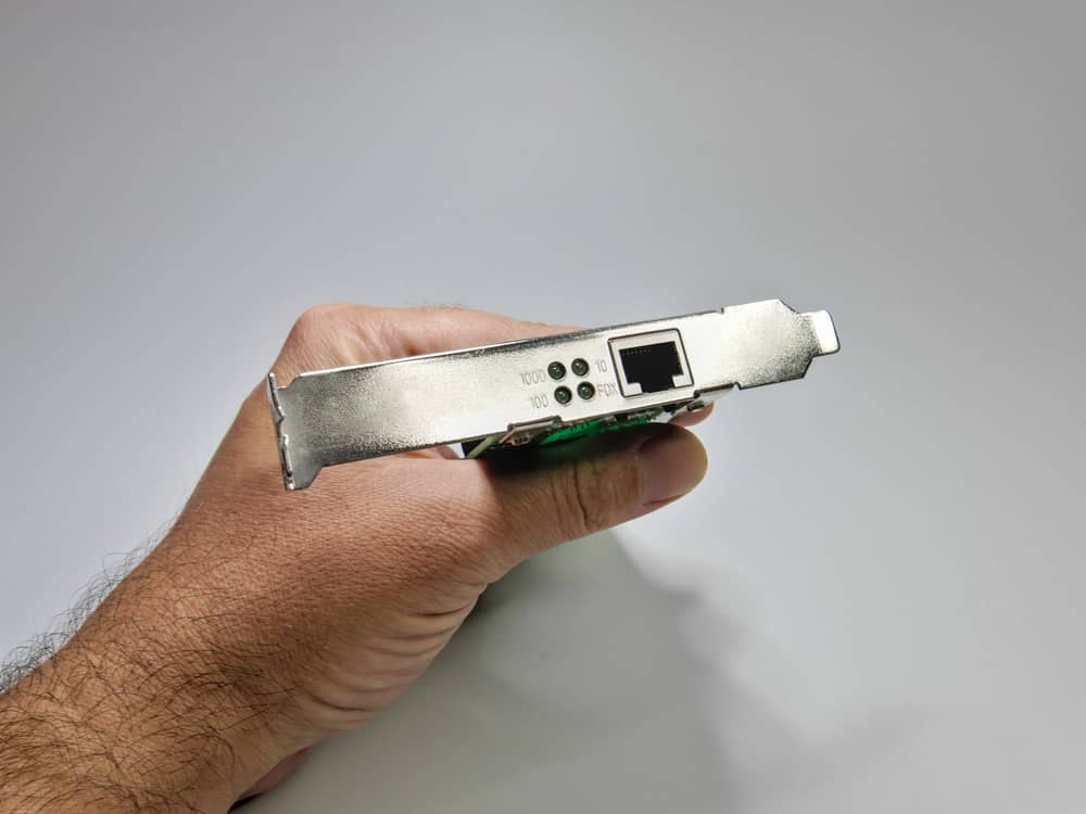 ¿Qué es un Adaptador de Red y para Qué Sirve? 7 Mano sujetando una tarjeta de red Ethernet PCI, mostrando el conector RJ45 y los indicadores LED.