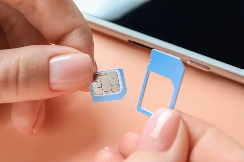 Reemplazar Tarjeta SIM: ¿Cuándo es Realmente Necesario? 3 Manos sosteniendo una tarjeta SIM y adaptándola a su adaptador. Se ve un teléfono inteligente en el fondo.