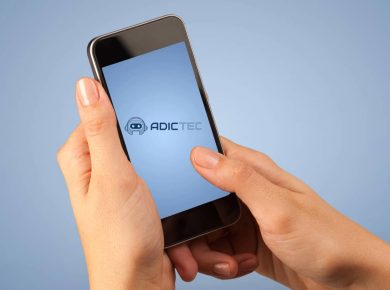 Cómo Apagar el iPhone sin tocar la Pantalla: Modelos con Touch ID y Face ID 7 Manos sosteniendo un iPhone con la pantalla encendida, mostrando el logotipo de Adictec.