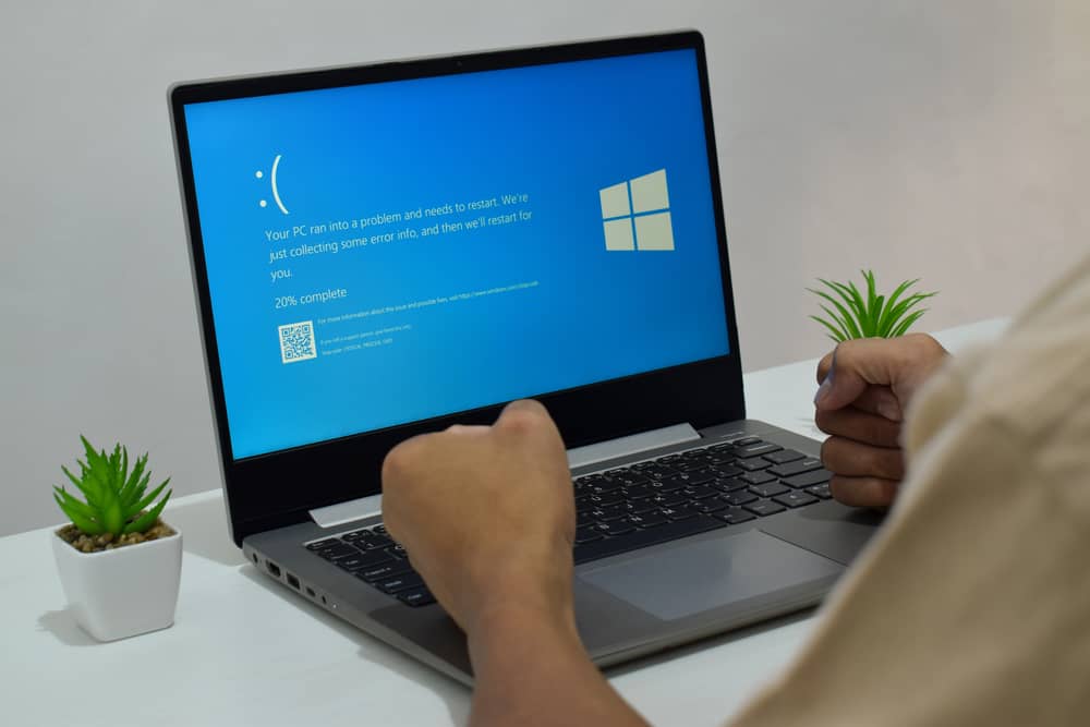 Mi PC se Reinicia Constantemente: ¡Solución Aquí! 6 Una persona con los puños cerrados frente a un portátil que indica mi PC se reinicia constantemente y no arranca, con el mensaje "Your PC ran into a problem and needs to restart".