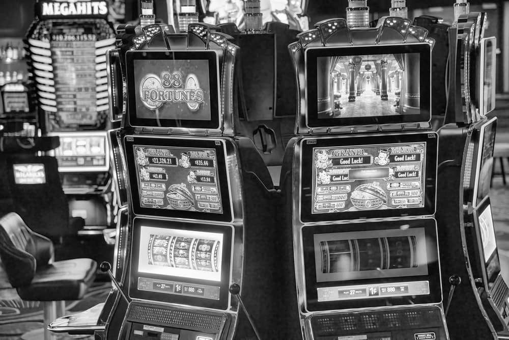 Historia y Evolución de las Máquinas Tragamonedas: De la Mecánica a lo Online 2 Foto en blanco y negro de un Ejemplo máquina tragamonedas mecánica moderna en un casino, mostrando pantallas digitales y detalles del juego.
