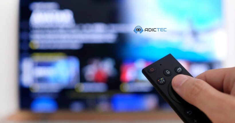 Mano sosteniendo un control remoto de TV frente a una pantalla desenfocada, simbolizando la elección de tu TV ideal entre QNED, QLED y OLED.